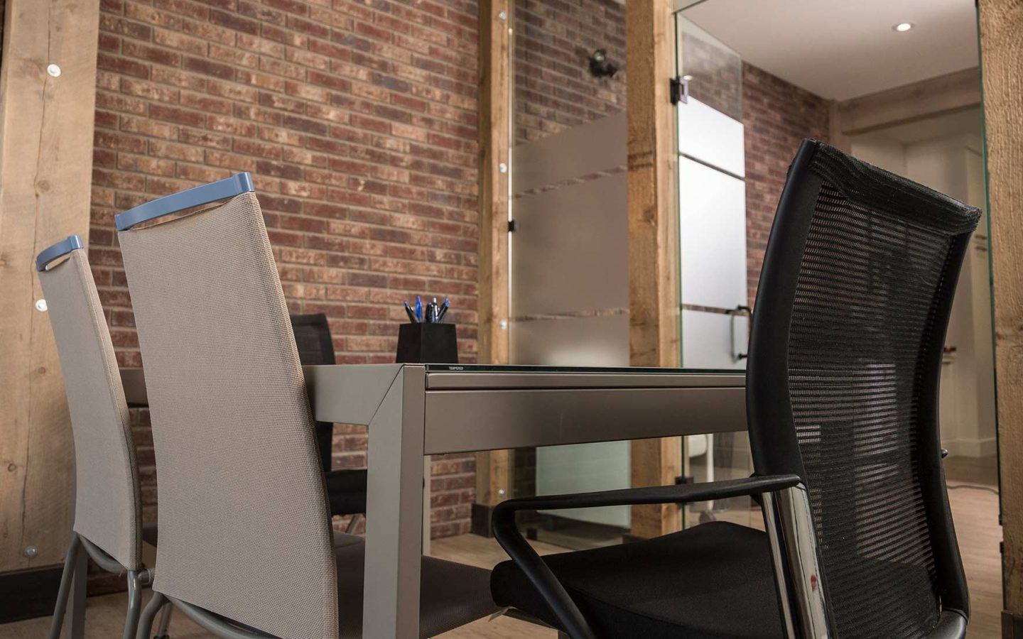 table surrounded by chairs in rustic office with wooden beams and brick walls