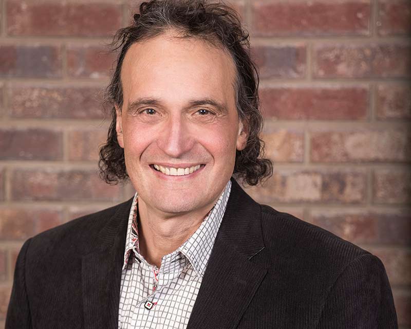 portrait of smiling man with long brown hair wearing suit and dress shirt