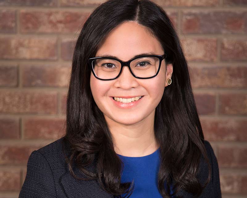 portrait of smiling woman with black rimmed glasses earring against brick wall